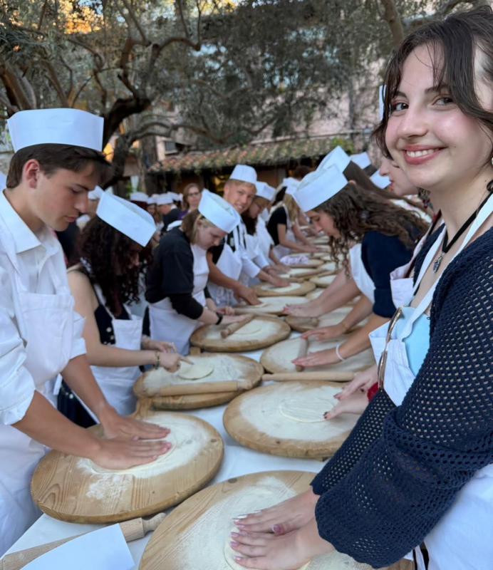 Students in a pizza making class line both sides of a long table, with each student kneading dough