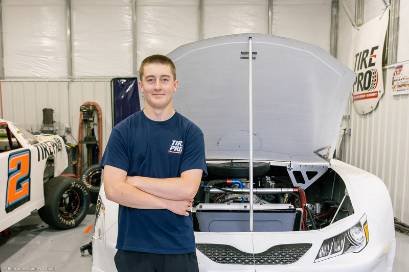 Canipe crosses his arms while standing in front of his car in the workshop.