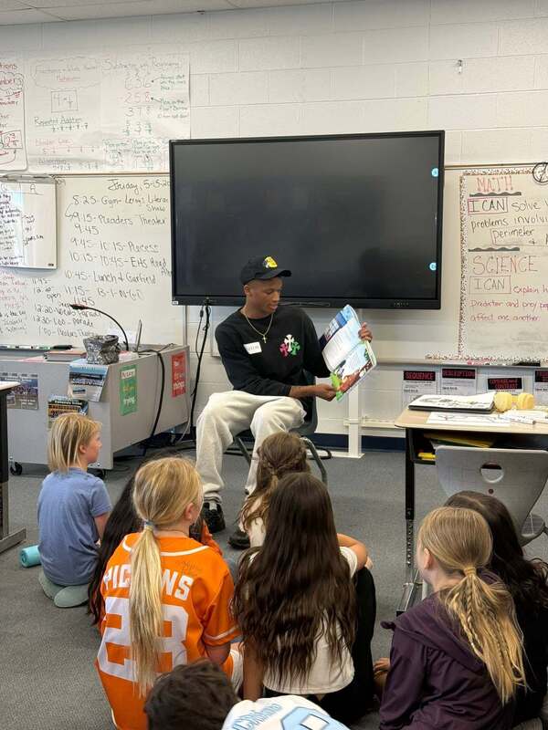 High school student reading a book to elementary kids.
