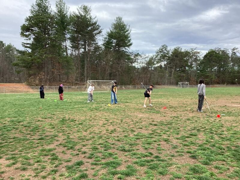 Students on a field practicing hitting golf balls.