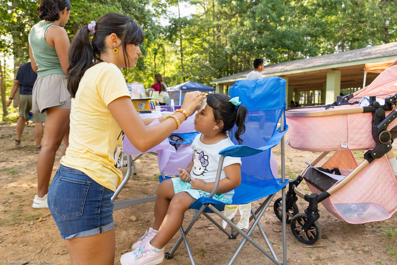 A girl gets her face painted while sitting in a chair.