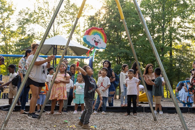 A boy swings at a pinata while a crowd watches.