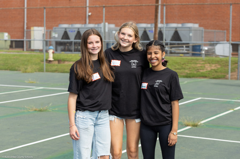 Three girls pose on a tennis court.