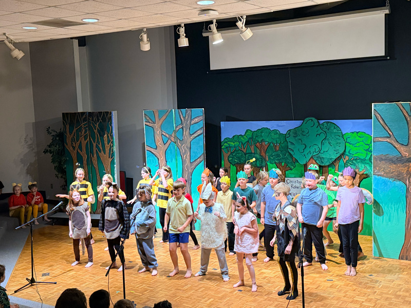 Group of students dressed up on stage singing and dancing. 