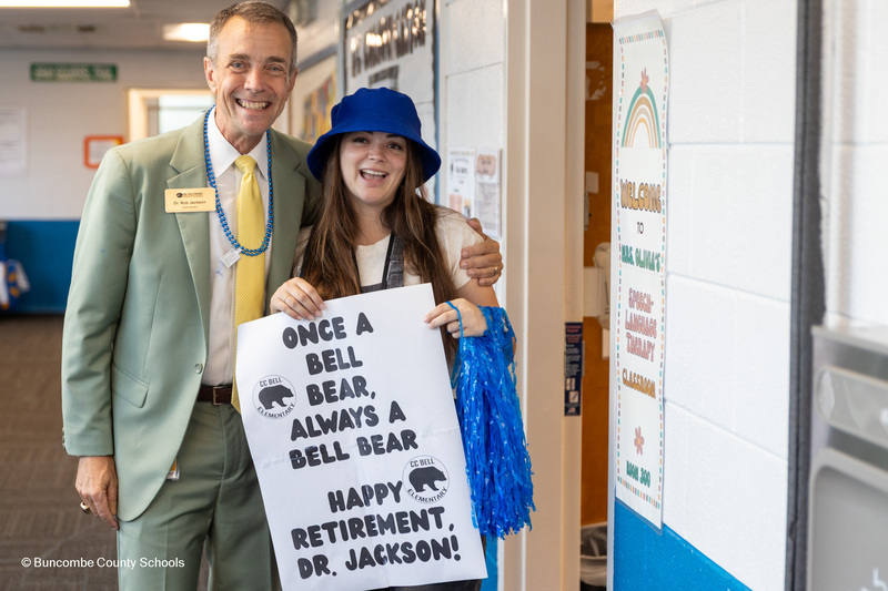 Dr. Jackson poses for a photo next to a teacher holding a sign "Once a Bell Bear, always a Bell Bear."