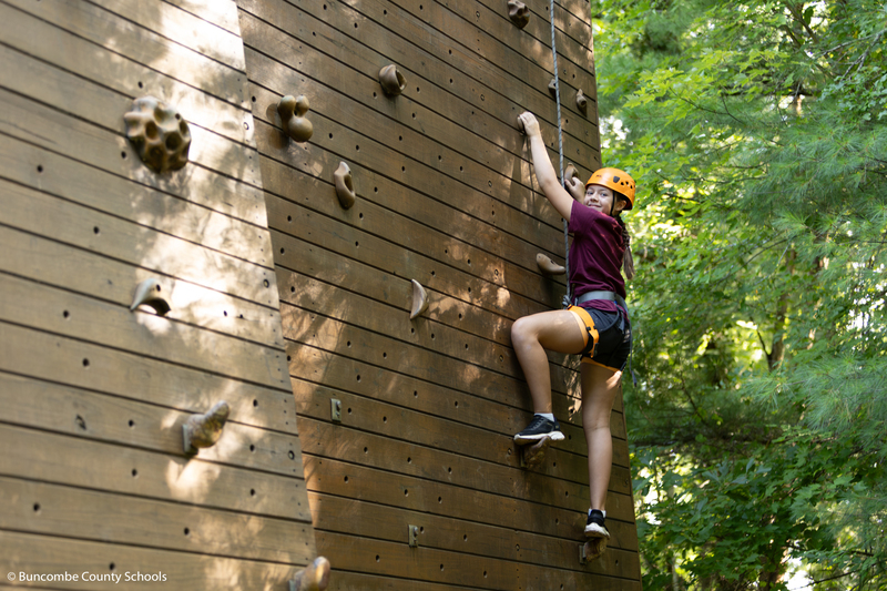Girl going up the climbing wall and smiling at the camera. 