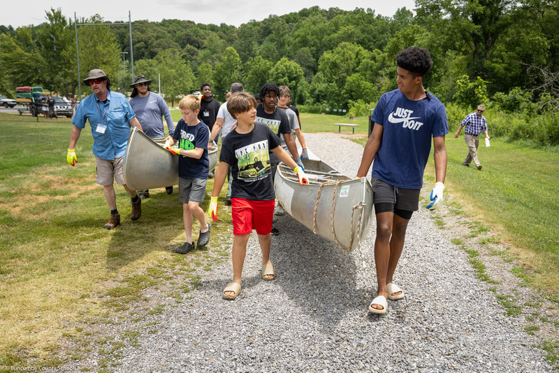 On-Track students carry canoes down a gravel path.
