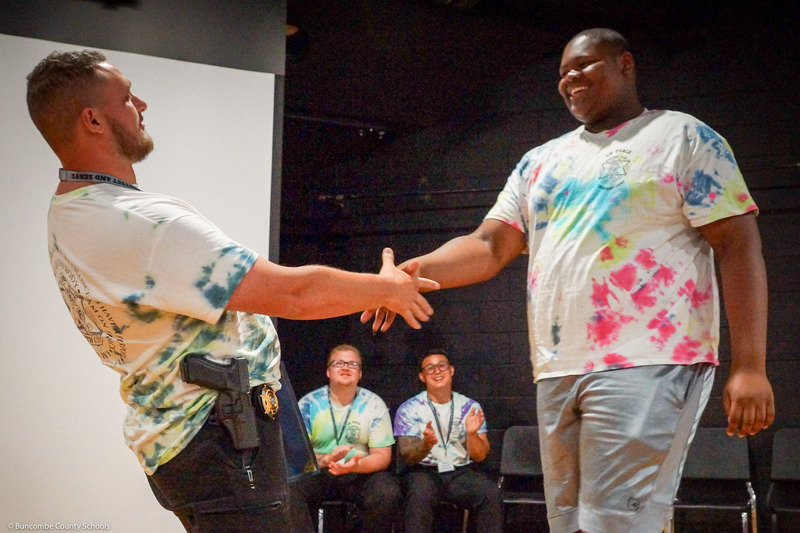 A boy in a tye-dye shirt shakes hands with an SRO.