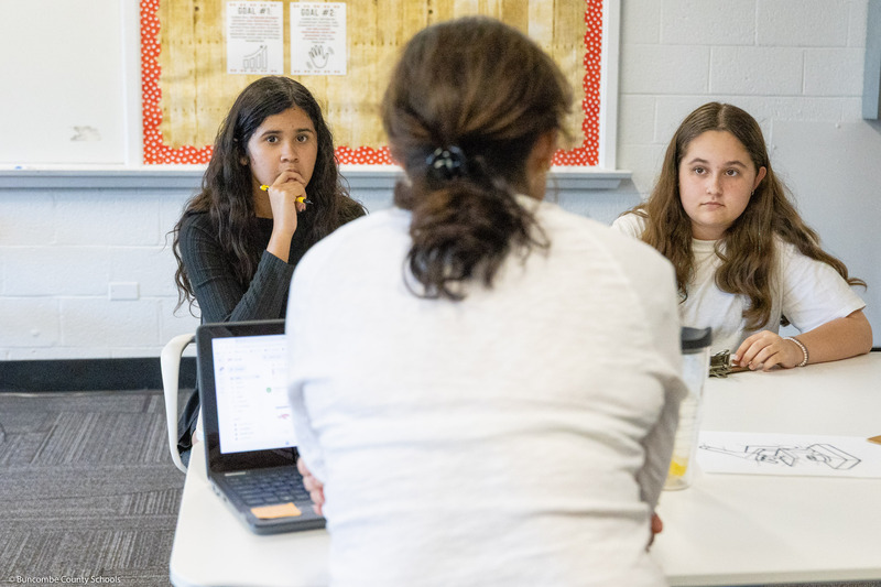 Two students listen while a teacher answers a question.