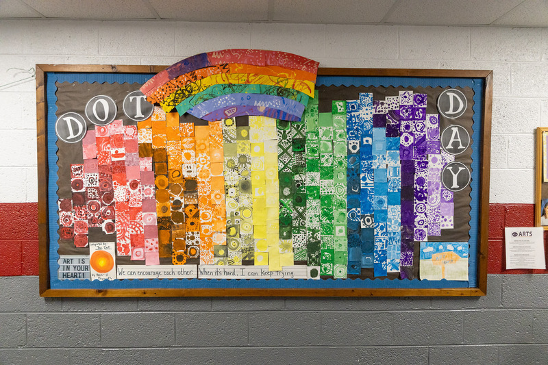 A wall outside the art classroom shows different colored 3-inch square tiles that make a rainbow.