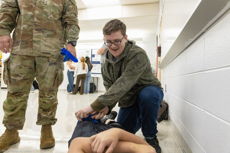 A student practices applying a tourniquet to another student while a member of the U.S. Army Traveling Medical Team supervises.