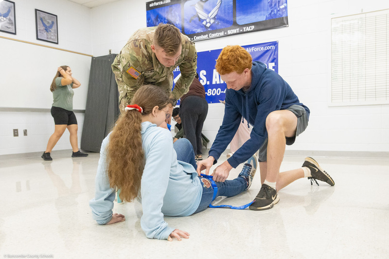 A student practices applying a tourniquet to another student while a member of the U.S. Army Traveling Medical Team supervises.
