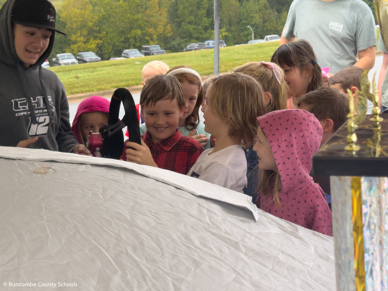 Students holding the steering wheel of a race car.