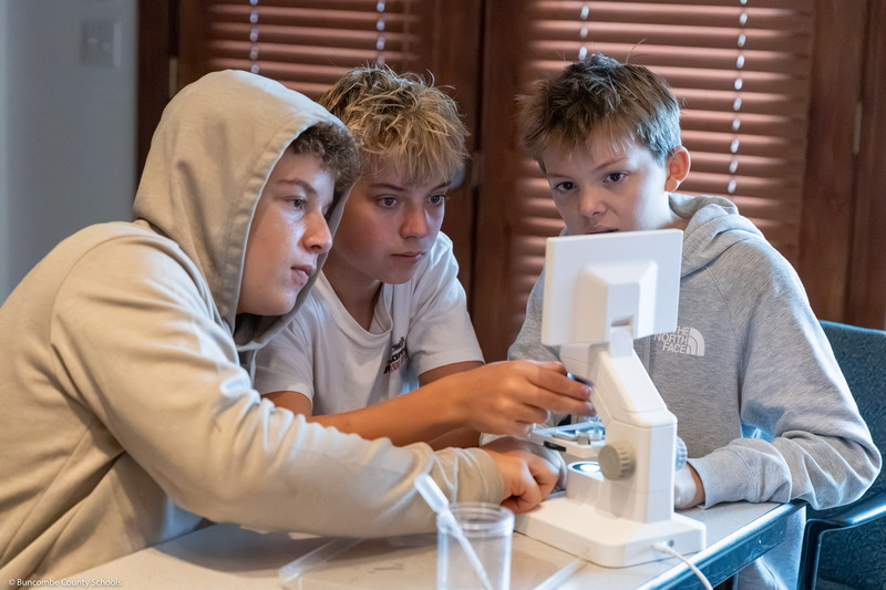 Three students look intently at a screen on a microscope.