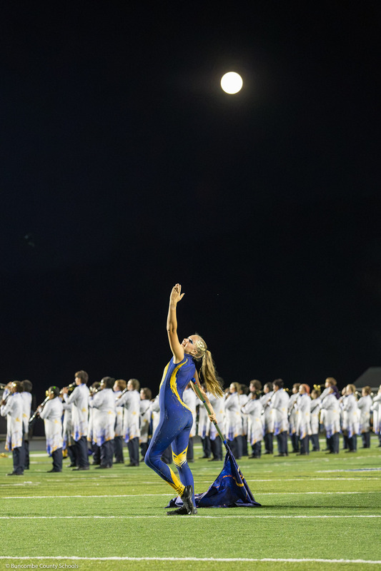 An Enka High color guard member points skyward while the moon hangs overhead.