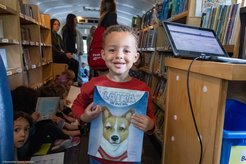 A pre-k student poses with a book in the Bookmobile.