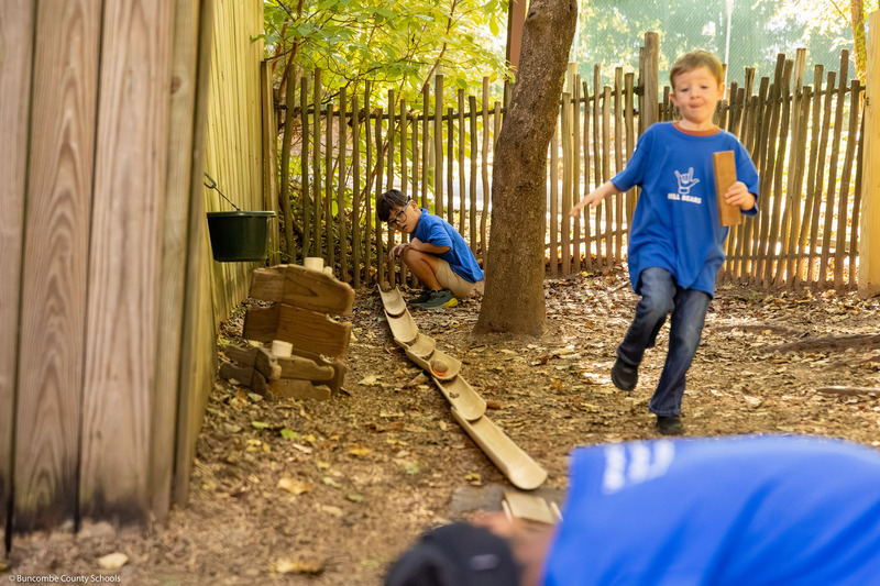 A boys rolls a ball down a shoot as another boy runs.