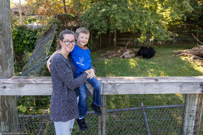 A mother holds her son with a black bear in the background.