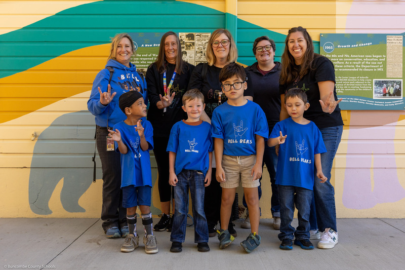 Four boys and five women pose as a group, some showing ASL signs.