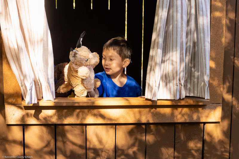 A boy holds up a puppet in a puppet stall.