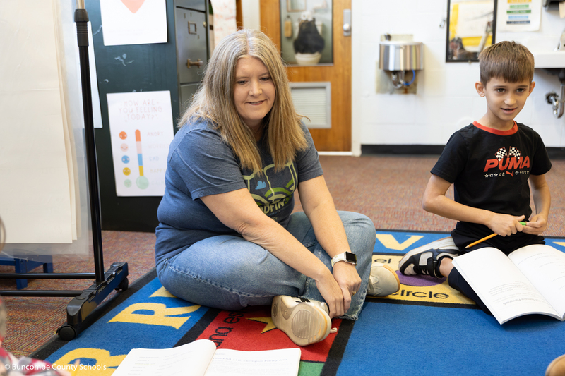 Ms. Wheeler sitting in the floor with students.