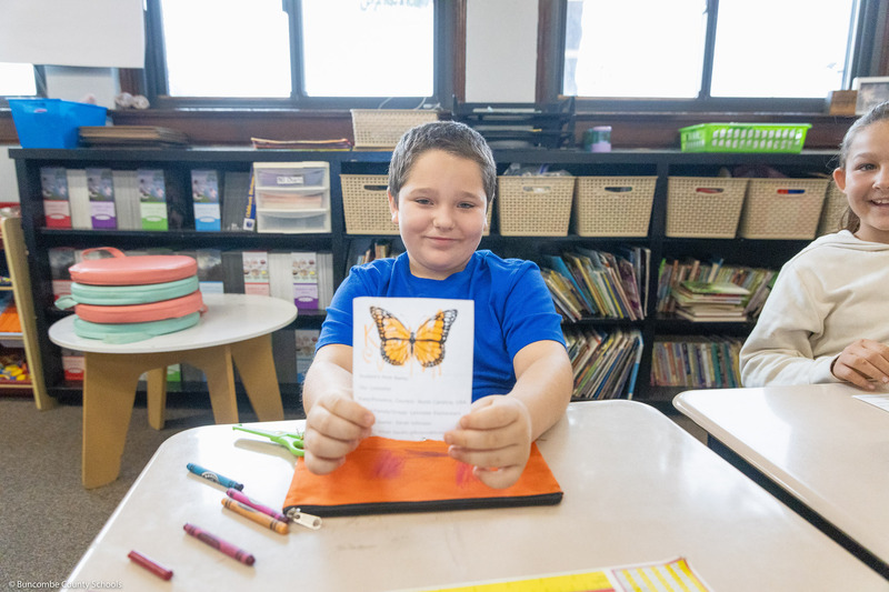 A boy shows off a life-sized monarch butterfly cutout.