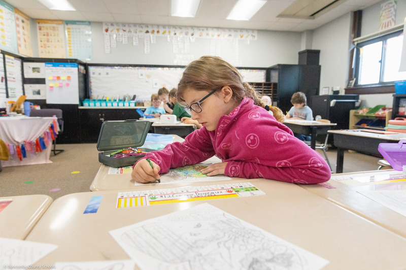 A girl colors a life-sized monarch butterfly cutout.