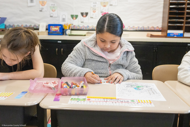 A girl colors a life-sized monarch butterfly cutout.