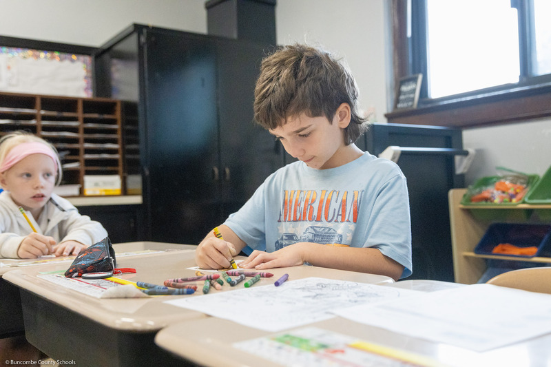 A boy colors a life-sized monarch butterfly cutout.