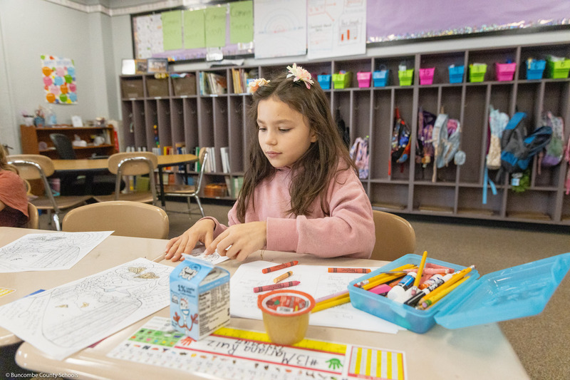A girl colors a life-sized monarch butterfly cutout.