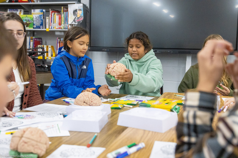 Two kids handle a brain model.
