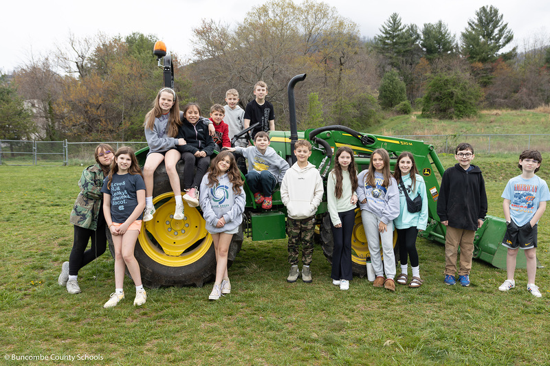 Students gathered around and sitting on a green and yellow tractor. 