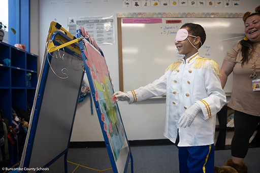 Boy wearing a blindfold and playing the game kiss the frog where he is playing paper lips on a frog. 
