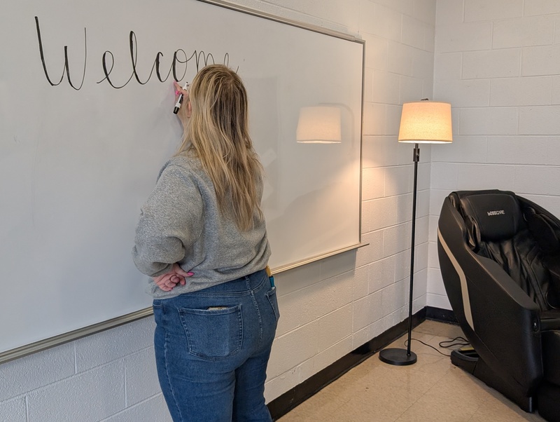 A Christos Foundation staffer writes "welcome" on a white board in the new serenity room. She's standing next to a new lamp and massage chair.