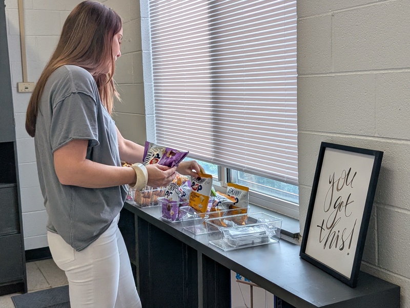 A Christos Foundation volunteer stocks bags of snacks in baskets on a shelf in the new serenity room. 
