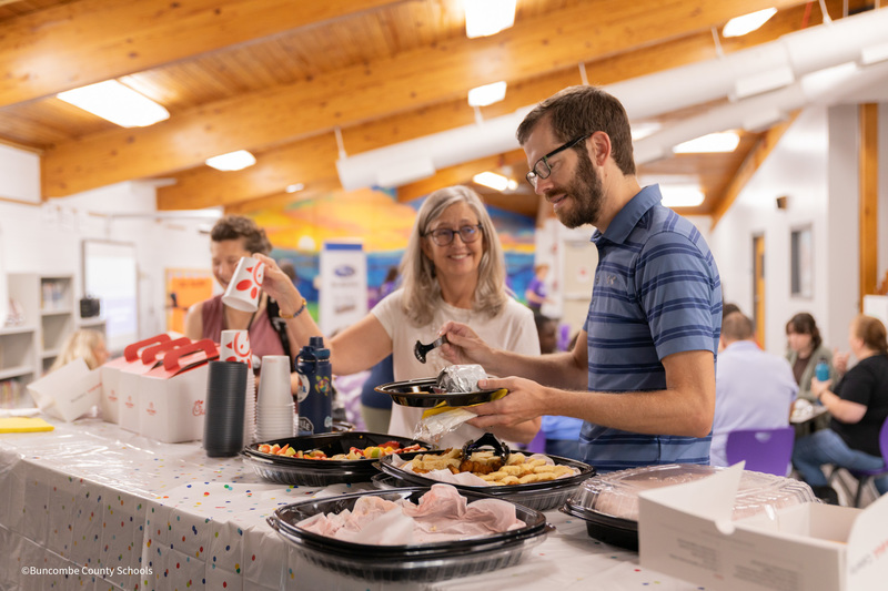 Two teachers stand in breakfast buffet line in the Emma Elementary media center