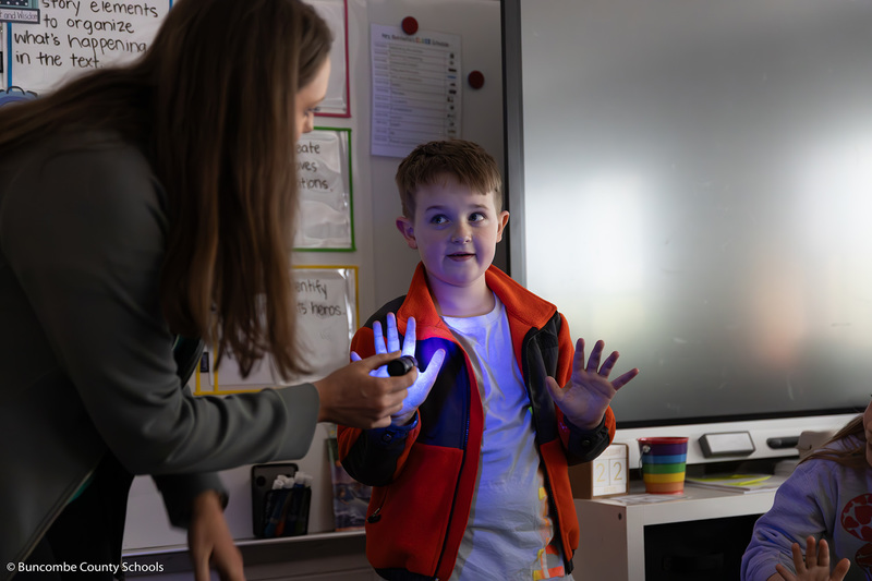 Instructor using a black light flashlight on a students hands to show how well he washed his hands before handling an egg. 