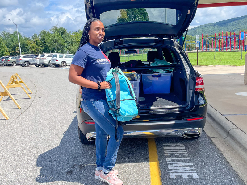 Sydney Ross unloads backpacks from the back of an open car parked in front of Hominy Valley Elementary