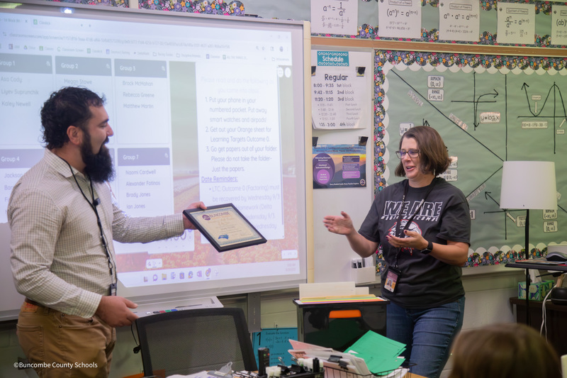 Mr. Arvey presents a certificate to Mrs. Stowe in her classroom