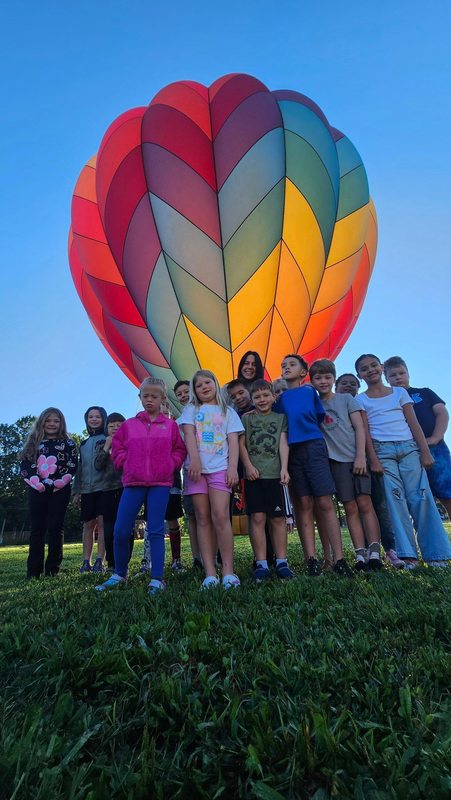 Group of students standing in front of the colorful hot air balloon. 