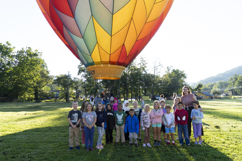A classroom of students and a teacher standing in front of the hot air balloon. 