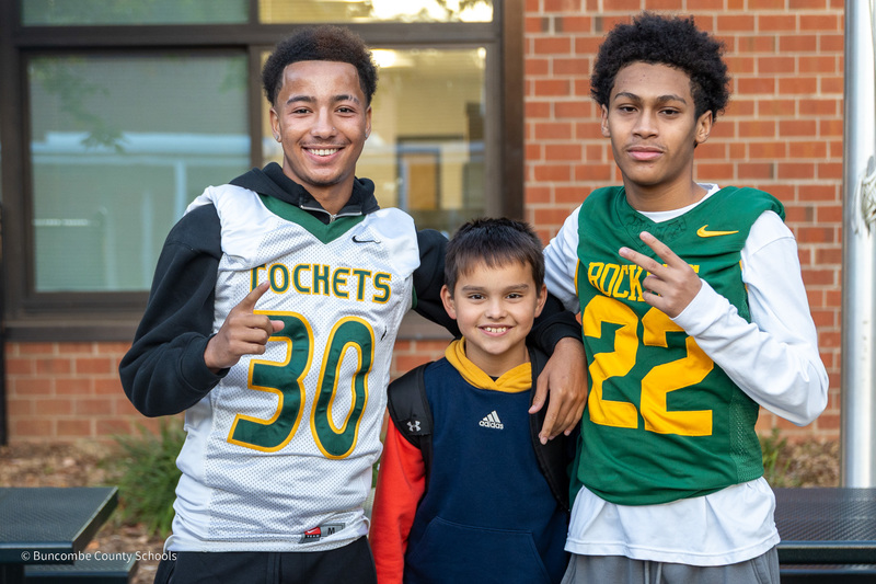 Reynolds football players Zion Ikeme and Jeremiah Jeter pose for a photo with a Haw Creek student standing between them on a sidewalk in front of the school