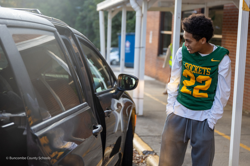 Reynolds football player smiles at child as the van door opens in the car rider line.