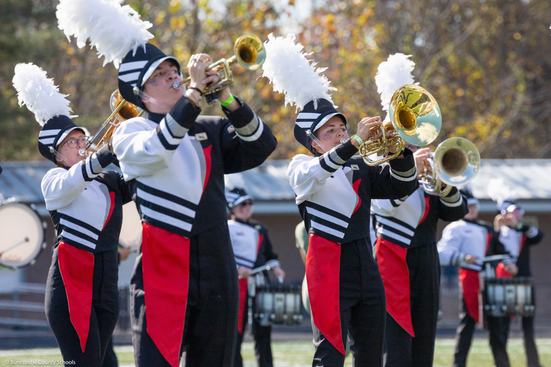 The North Buncombe High marching band, dressed in black, red, and white, playing horns during a marching band show.