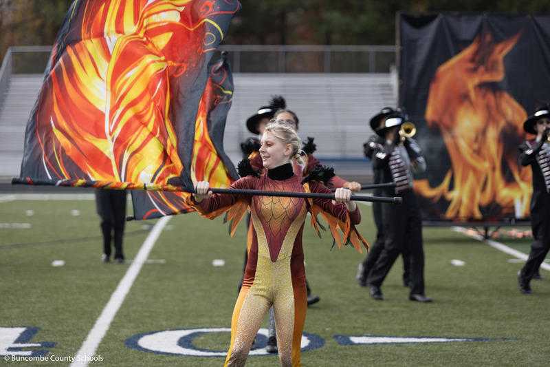 Owen High color guard member with a flag resembling a flame performs in front of the school marching band's trumpet section.