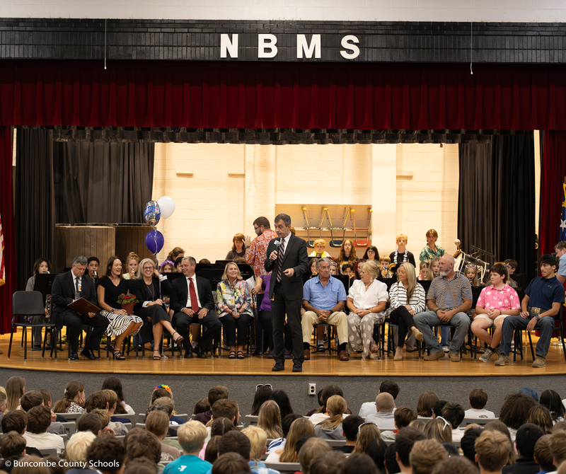 Dr. Jackson stands on stage addressing the students and staff. BCS school leaders and Mr. Honeycutt's family is seated on stage behind him.