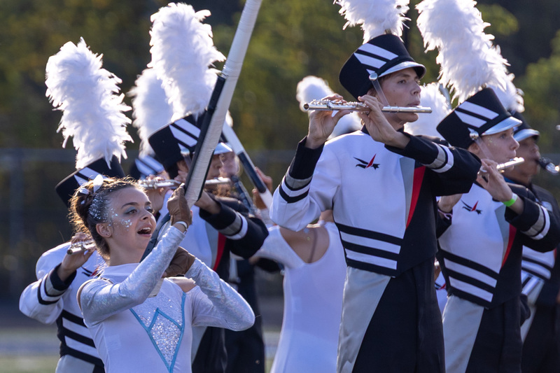 Color guard and flute players in full band uniform play on the field.