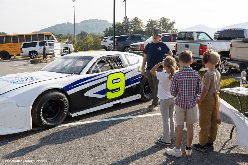 High school student talking to group of students about his race car. 