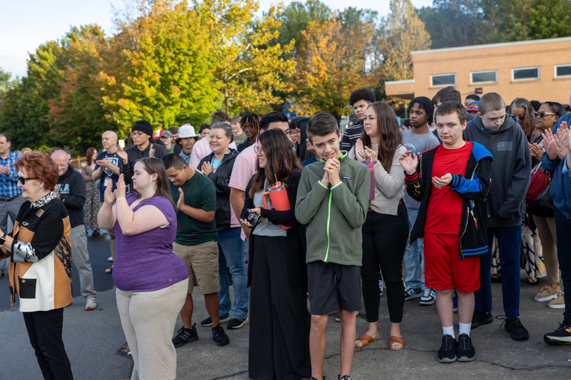 A crowd of students standing outside claps for Mr. Harbin