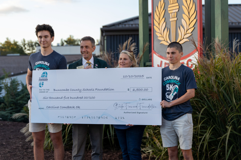 Matthew, Superintendent Dr. Rob Jackson, Christy Cheek, and Pablo hold the giant check outside of the Reynolds stadium